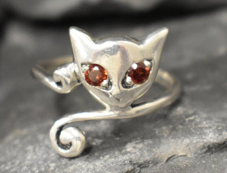 May include: A silver ring with a cat design. The cat has red gemstone eyes.