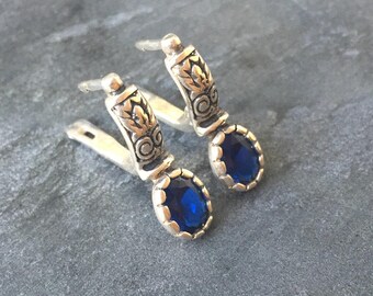 May include: A pair of silver earrings with blue gemstone accents. The earrings feature a floral design and a dangling blue stone.