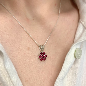 May include: A silver chain necklace with a pendant featuring a cluster of small, red gemstones set in a flower shape.