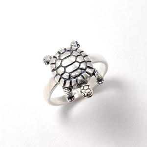 May include: A silver ring with a detailed turtle design. The turtle is facing upwards with its legs and head visible.