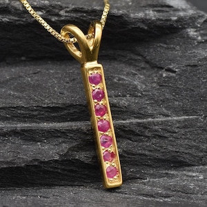May include: A gold pendant necklace with a vertical bar set with eight small pink gemstones.