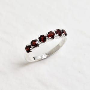 May include: A silver band ring with six red garnet stones set in a row.