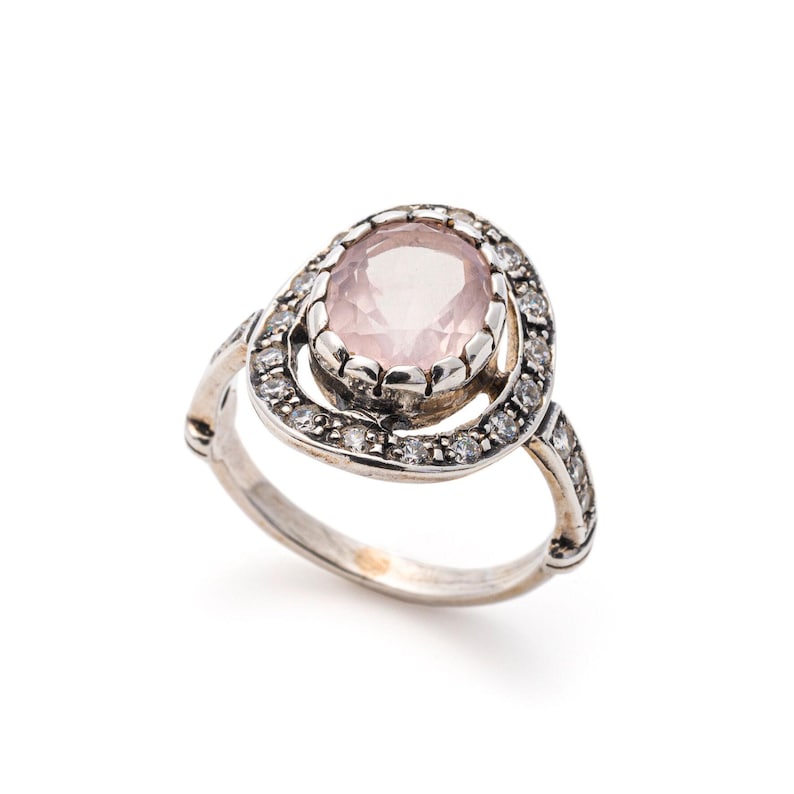 May include: A silver ring featuring a pink oval gemstone set within a halo of smaller clear gemstones.