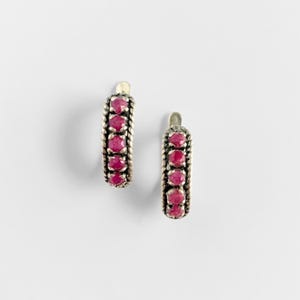 May include: A pair of hoop earrings featuring a twisted metal border and four round, deep pink rubies set in a vertical row on each earring. The metal has a darkened, oxidised finish that highlights the textured rope-like detailing.