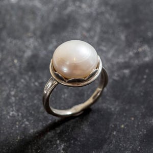 May include: A silver ring with a large, white pearl set in a scalloped bezel.