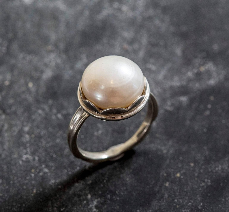 May include: A silver ring with a large, white pearl set in a scalloped bezel.