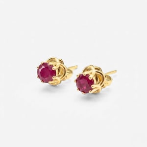 May include: A pair of gold stud earrings, each featuring a vibrant red gemstone. The earrings have a detailed, floral-inspired setting. The gemstones are round and appear to be approximately 0.25 inches in diameter.