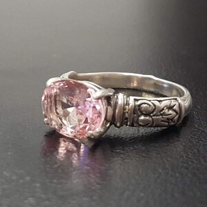 May include: A silver ring with an oval-shaped pink gemstone set in a detailed silver band.