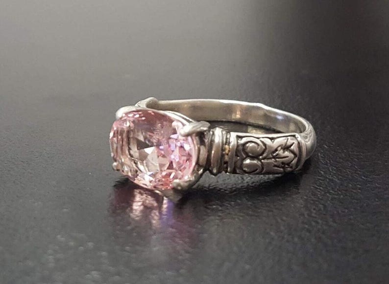May include: A silver ring with an oval-shaped pink gemstone set in a detailed silver band.