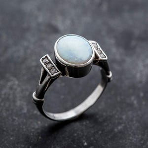 May include: A silver ring with a white opal gemstone and small diamonds on the band.
