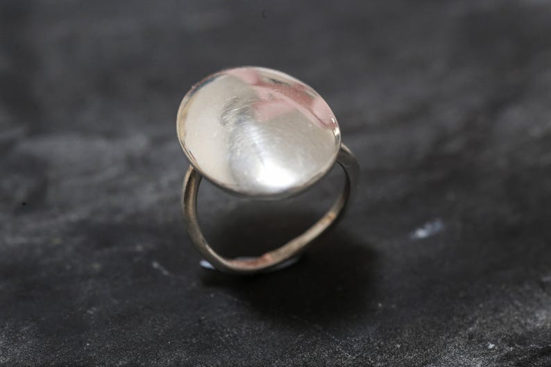 May include: A silver ring with a smooth, oval-shaped top.