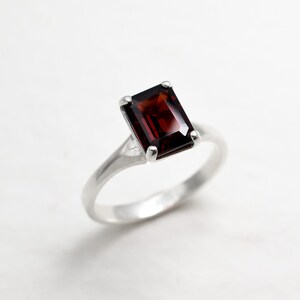 May include: A silver ring with a dark red, emerald-cut gemstone.
