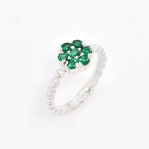 Può includere: Un anello d'argento con un gruppo di pietre preziose verdi rotonde disposte a forma di fiore. La fascia presenta un motivo strutturato con piccole perle distanziate. L'anello è posto su uno sfondo bianco.