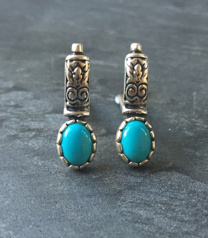 May include: A pair of silver earrings with turquoise stones. The earrings have a decorative design on the top part and a round turquoise stone at the bottom.