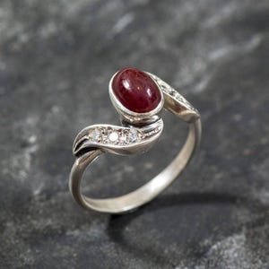 Peut inclure: Une bague en argent avec une pierre précieuse rouge et de petites pierres claires serties dans un motif en spirale.