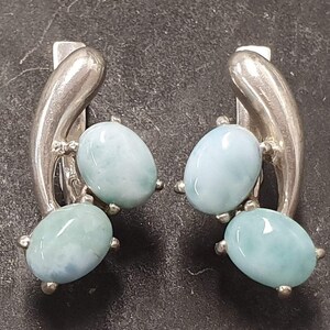 May include: A pair of silver earrings with three blue-green gemstone accents each. The earrings are shaped like a curved line.