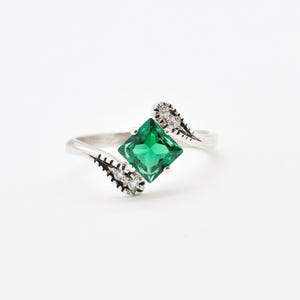 May include: A silver ring with a square green gemstone and smaller clear gemstones on the band.