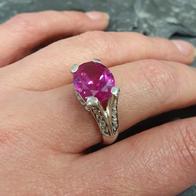 May include: A silver ring with a large oval-shaped pink gemstone surrounded by smaller clear gemstones.