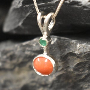 Puede incluir: Un collar con un colgante de plata, adornado con una piedra redonda de coral naranja y una peque&ntilde;a piedra redonda de esmeralda verde.