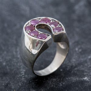May include: A silver ring with a horseshoe design set with pink gemstones. The ring is thick and has a rounded band.