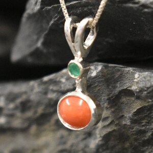 Puede incluir: Un colgante de plata con una piedra redonda de coral naranja y una piedra redonda verde m&aacute;s peque&ntilde;a.