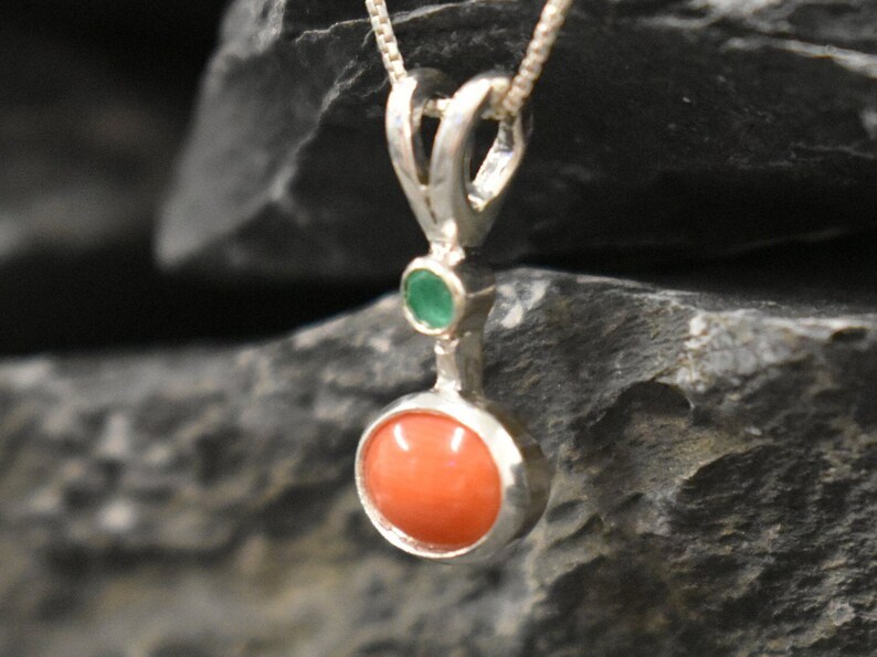 Puede incluir: Un colgante de plata con una piedra redonda de coral naranja y una piedra redonda verde m&aacute;s peque&ntilde;a.