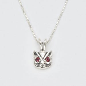 Peut inclure: Un collier en argent avec un pendentif en forme de chat avec des yeux en pierres précieuses rouges.