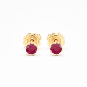 May include: A pair of gold stud earrings with small, round, red ruby gemstones.