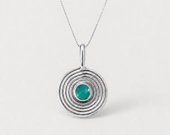 Könnte beinhalten: Eine silberne Halskette mit einem kreisförmigen Anhänger, der konzentrische, gerillte Ringe und einen kleinen, runden, glatten, türkisfarbenen Stein in der Mitte aufweist. Der Anhänger hängt an einer zarten, dünnen Silberkette mit poliertem Finish.
