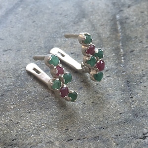 May include: A pair of silver earrings with a curved design featuring alternating green and red gemstones.