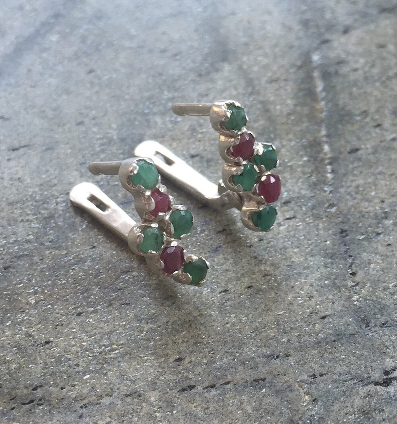 May include: A pair of silver earrings with a curved design featuring alternating green and red gemstones.