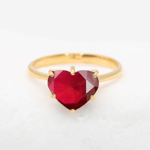 May include: A gold ring featuring a large, red heart-shaped gemstone.