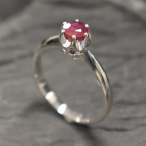 Könnte beinhalten: Ein silberner Ring mit einem roten Rubin-Edelstein in einer Krappenfassung.