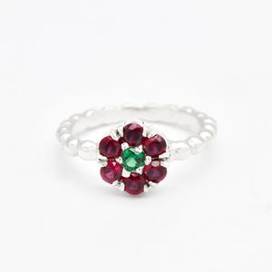 Peut inclure: Une bague en argent avec un motif de fleur rouge et verte. La fleur a un centre vert et est entourée de pierres rouges.