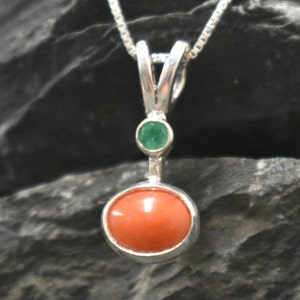 Puede incluir: Un collar con un colgante de plata, adornado con una piedra redonda de coral naranja y una peque&ntilde;a piedra redonda de esmeralda verde.