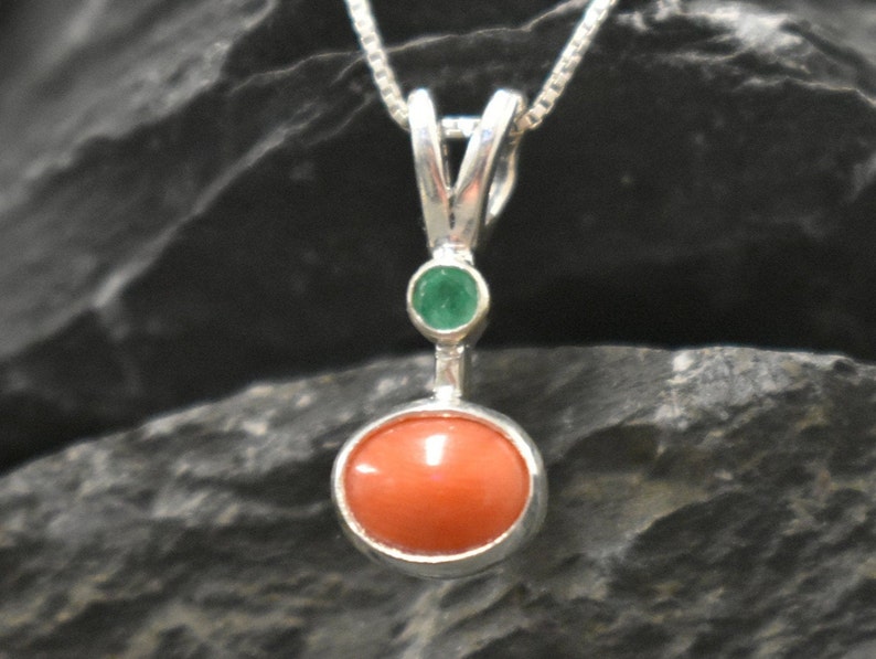 Puede incluir: Un collar con un colgante de plata, adornado con una piedra redonda de coral naranja y una peque&ntilde;a piedra redonda de esmeralda verde.