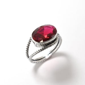 May include: A silver ring with a twisted band and a large oval-shaped red gemstone.