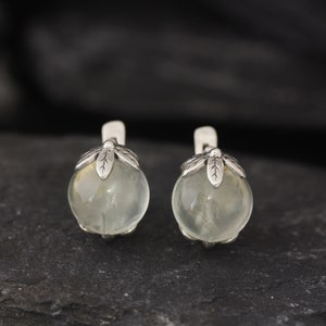 May include: A pair of silver earrings with clear round stones and leaf-shaped accents.