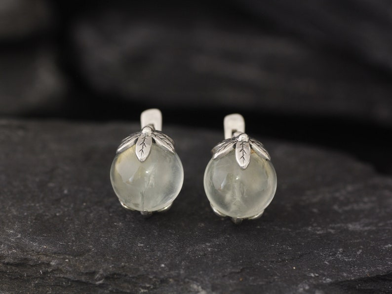 May include: A pair of silver earrings with clear round stones and leaf-shaped accents.