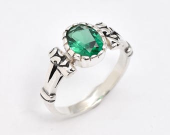 May include: A silver ring featuring an oval, emerald-green gemstone. The ring has an ornate, detailed design on the band and around the gemstone setting. The gemstone is the focal point, set in a bezel setting, and the ring is displayed against a white background.