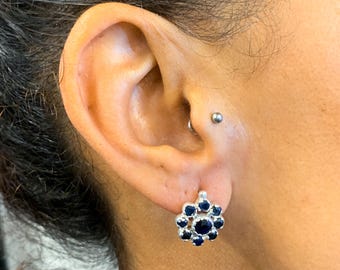 Puede incluir: Un par de pendientes de plata con un racimo de piedras preciosas azul oscuro en forma de flor.