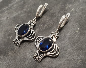 May include: A pair of silver earrings with intricate designs and blue gemstone accents.