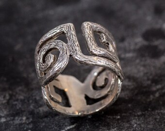 Könnte beinhalten: Ein silberner Ring mit einem strukturierten, komplizierten Design, das ein sich wiederholendes Muster aus Spiralen und Quadraten aufweist.