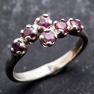 May include: A silver ring with a curved row of six small, deep pink gemstones.