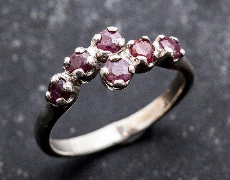 May include: A silver ring with a curved row of six small, deep pink gemstones.