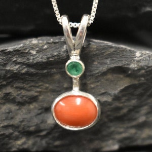 Puede incluir: Un collar con un colgante de plata, una piedra redonda de coral naranja y una peque&ntilde;a piedra redonda verde.