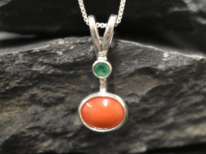 Puede incluir: Un collar con un colgante de plata, una piedra redonda de coral naranja y una peque&ntilde;a piedra redonda verde.
