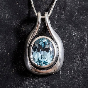 May include: A silver pendant necklace with a light blue oval gemstone set in a silver bezel. The pendant is shaped like a teardrop and has a smooth, polished finish.
