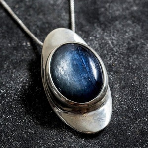 May include: A silver pendant necklace with a blue gemstone set in a silver oval frame.