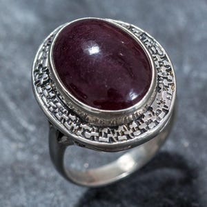 May include: A silver ring with an oval-shaped, dark red gemstone set in a detailed, textured band.